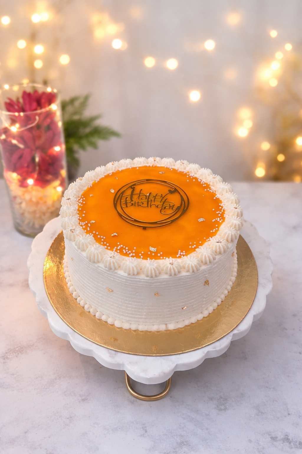 Mango mirror glaze cake on a marble cake stand with warm bokeh lights